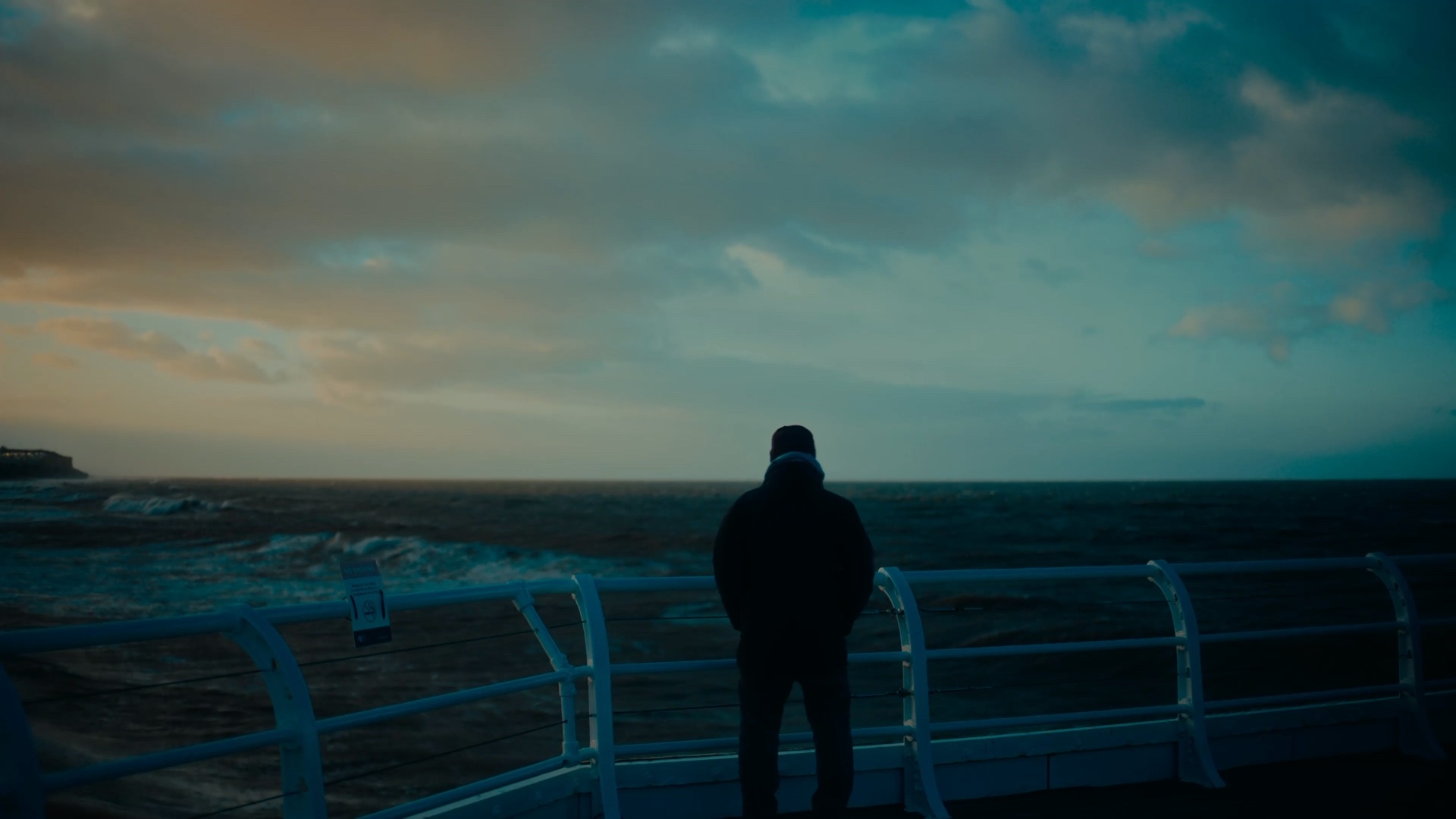 A figure at a seafront railing, watching a winter sea